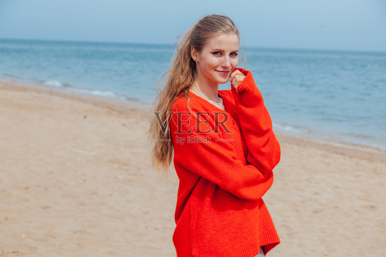 那个穿红衣服的金发女郎沿着海边的海滩散步照片摄影图片