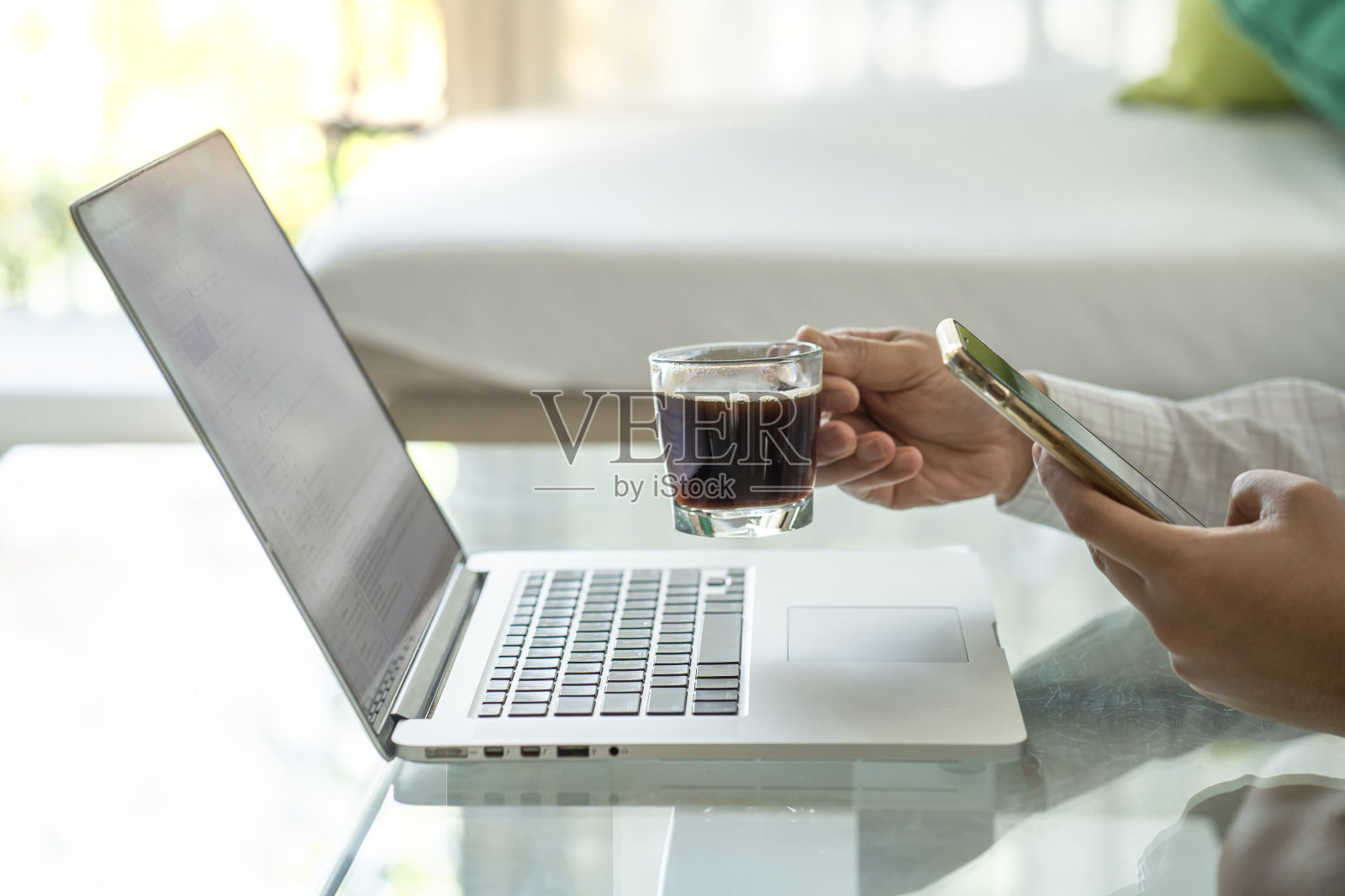 在花冠病毒隔离期间使用智能手机和笔记本电脑在家工作的男子。照片摄影图片