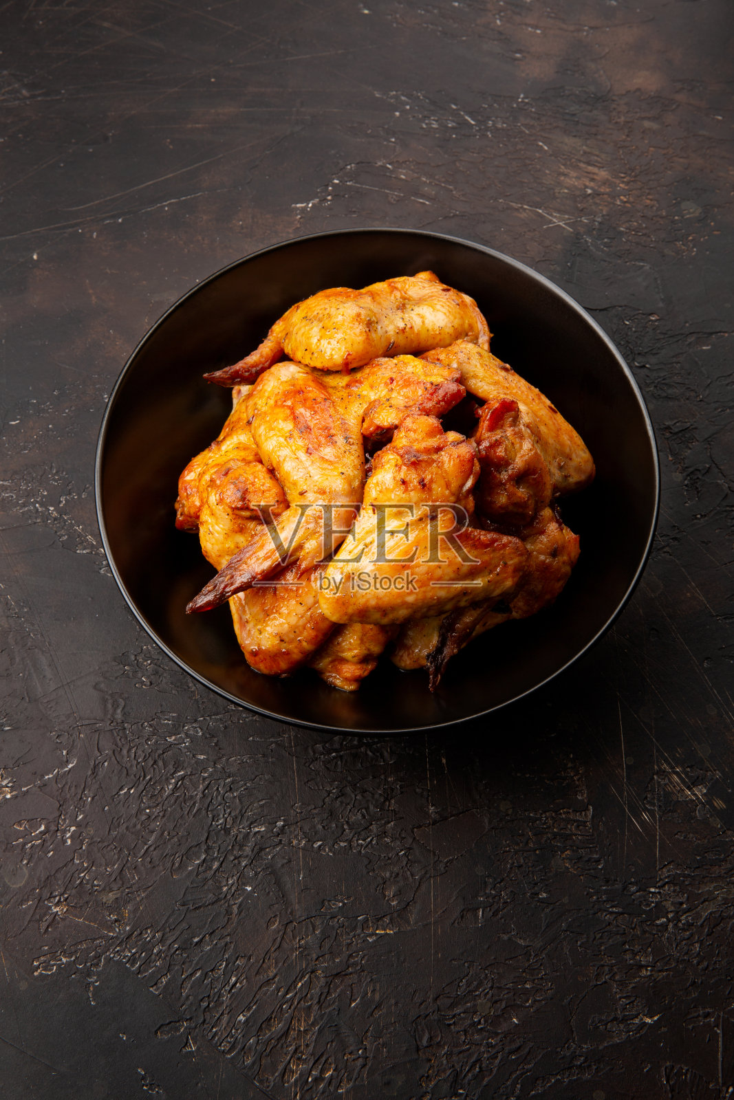 烤鸡翅膀在黑色的盘子上，在黑色的背景照片摄影图片
