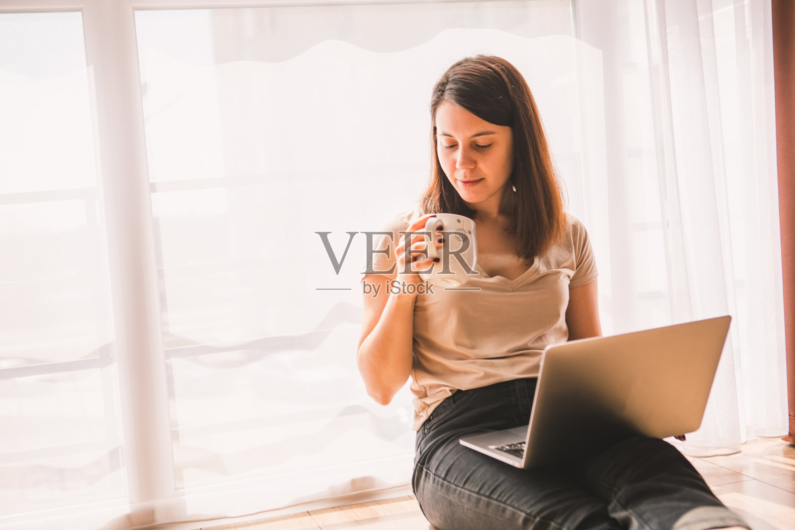 坐在地板上用笔记本电脑工作的女人靠近大窗户照片摄影图片