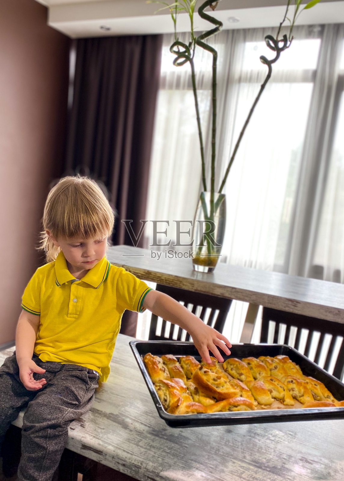 皮肤白皙的孩子正在吃撒了糖粉的新鲜烤面包。照片摄影图片