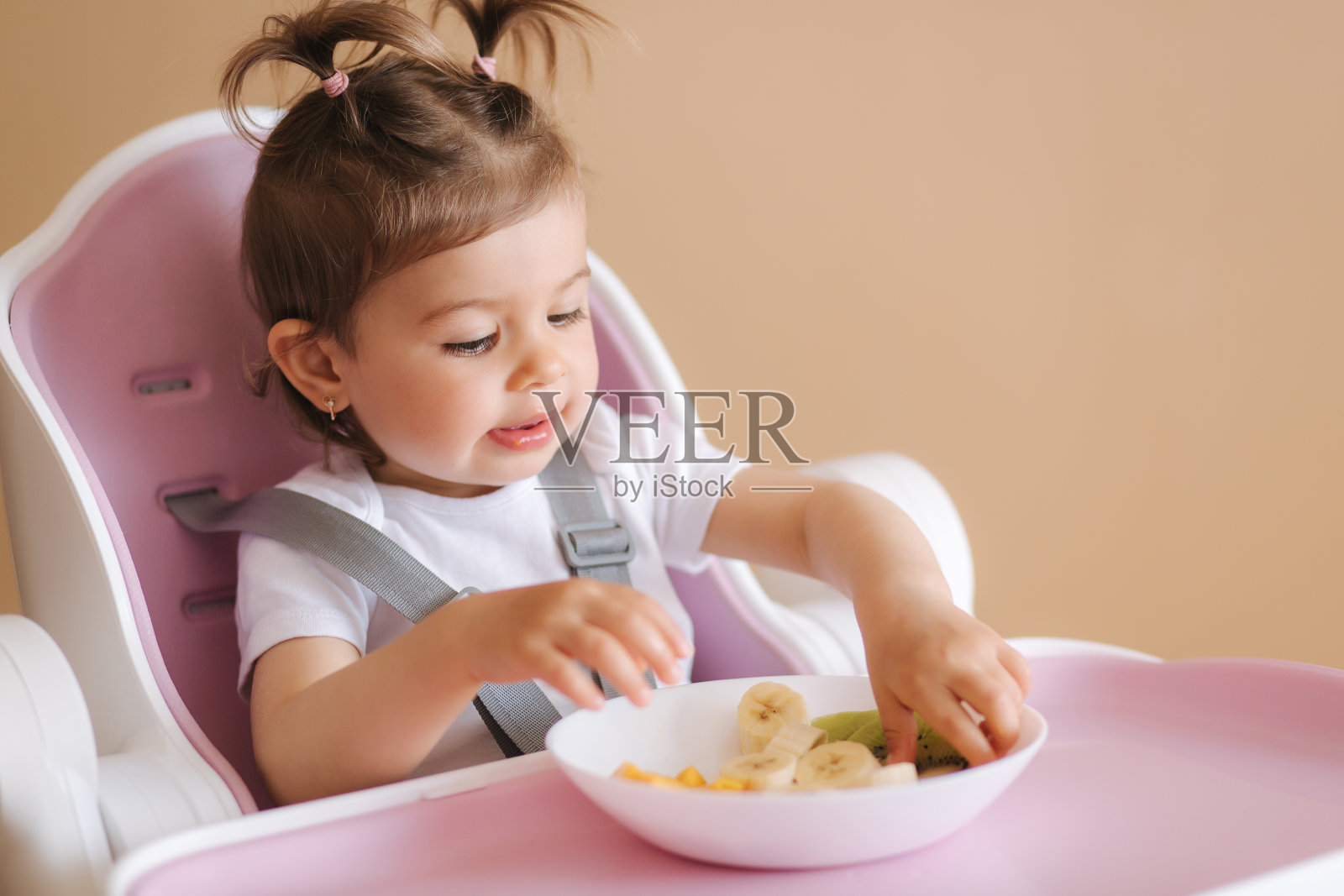 快乐的小女婴在高椅子上吃异国水果的肖像。儿童健康营养照片摄影图片