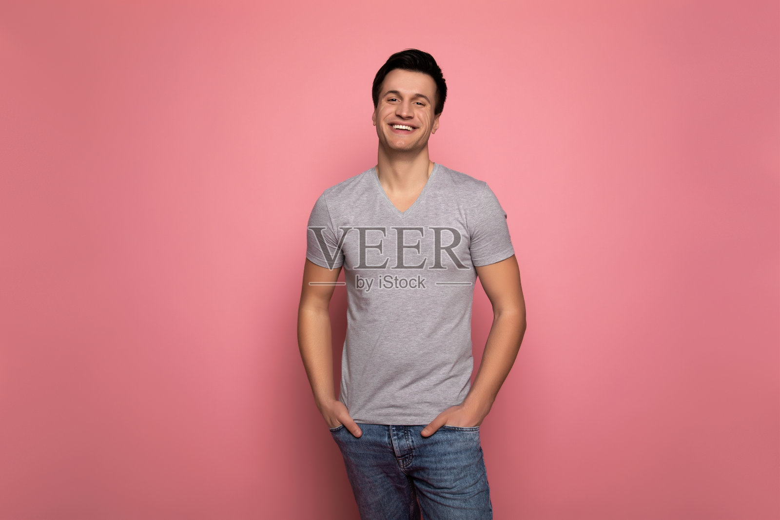 世界上最幸福的人。一个开朗的年轻人穿着休闲装看着镜头，同时自信地把他的手放在口袋里。照片摄影图片