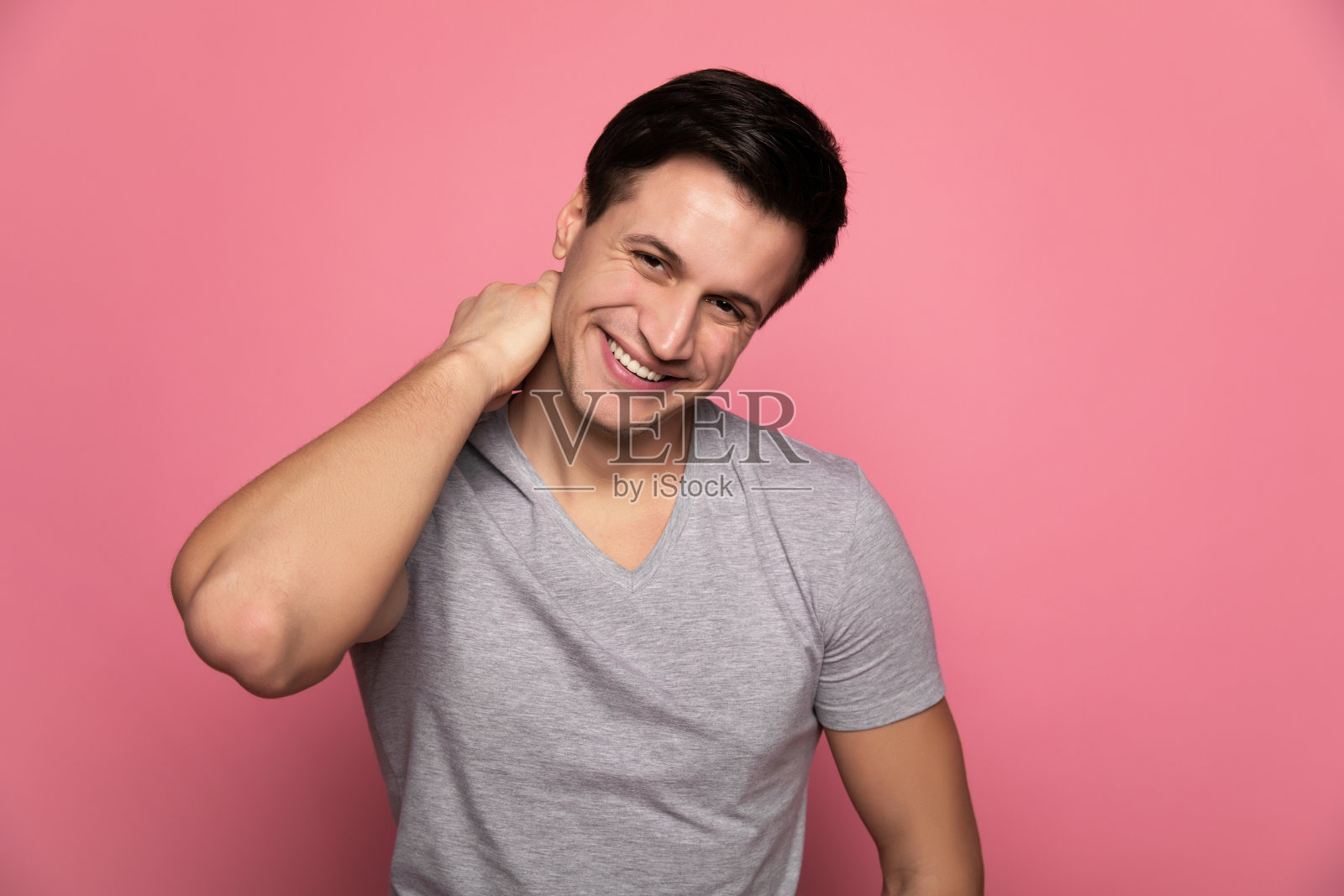 有魅力的人。一个快乐的年轻人的特写照片，他看着相机，同时用他的右手触摸他的脖子。照片摄影图片