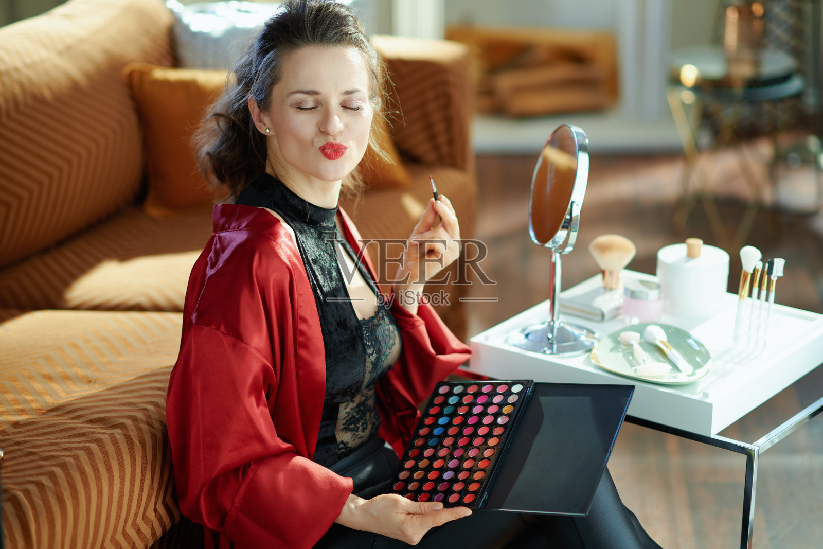 在阳光明媚的日子里，时尚女性在现代家居中涂上唇膏照片摄影图片