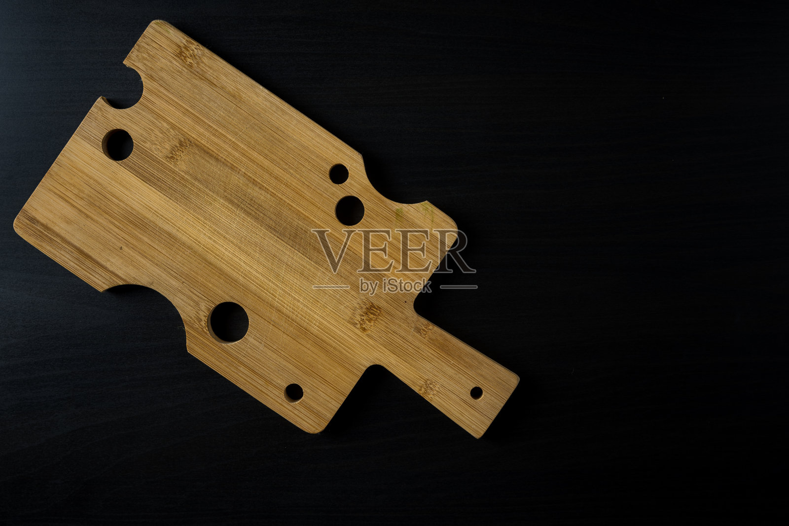 由浅色木材制成的切菜板，在深色木质背景上有像奶酪一样的孔，文字区照片摄影图片