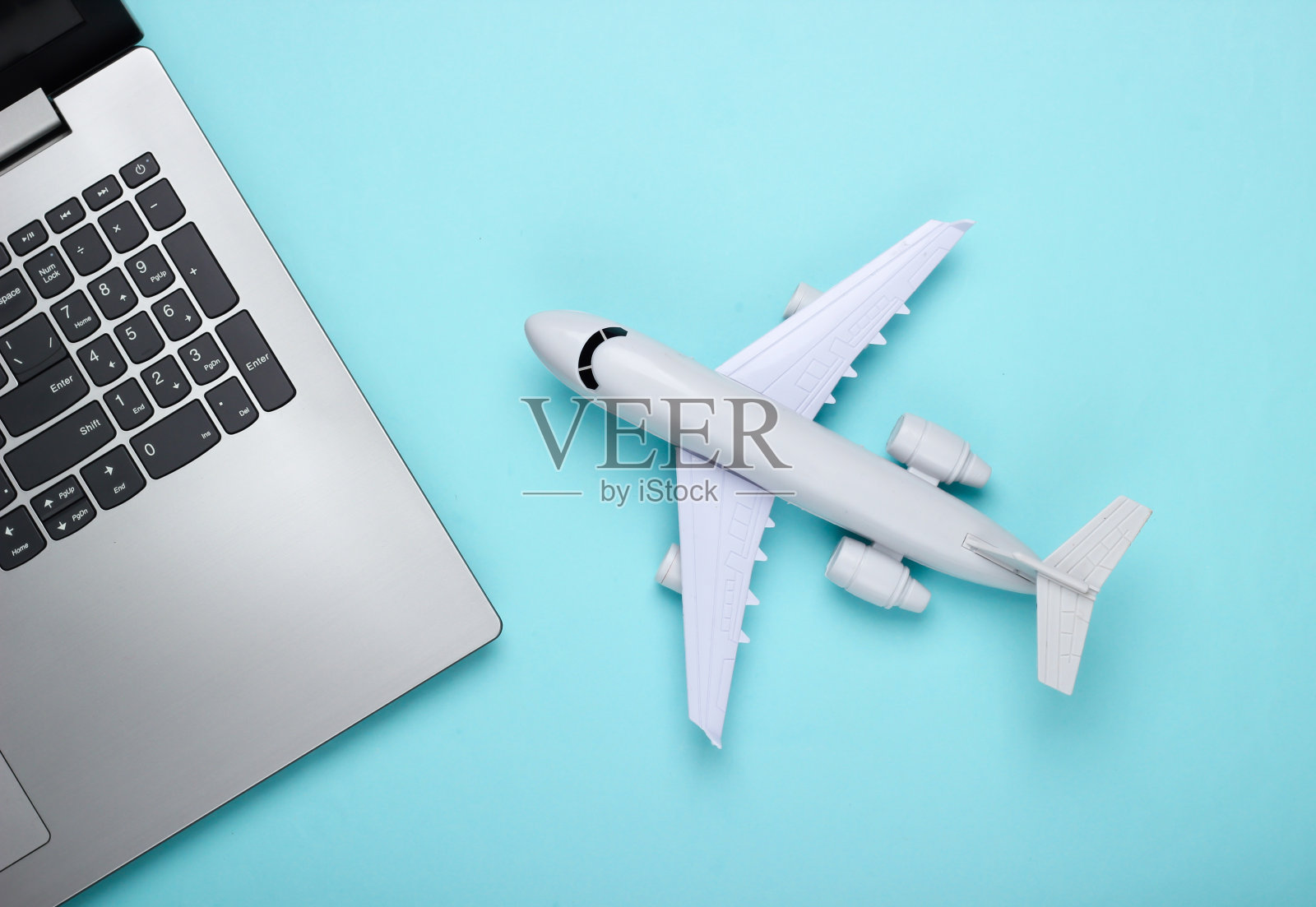 网上订票。选择旅游目的地。蓝色粉彩背景上的笔记本电脑和飞机雕像。俯视图照片摄影图片