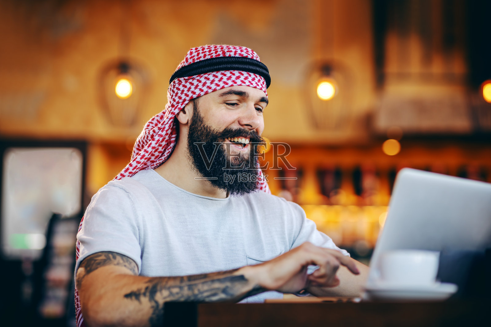 在咖啡馆使用笔记本电脑上网的年轻穆斯林男子照片摄影图片