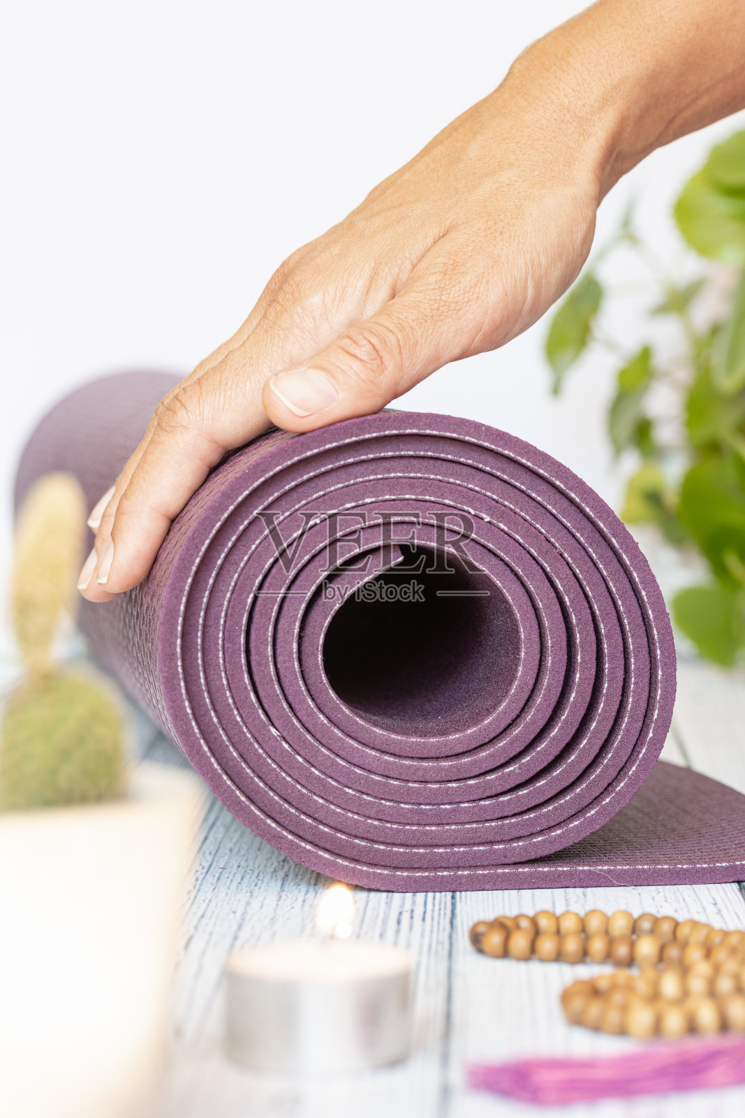 一个女人的手展开紫色瑜伽垫的特写，坏的木珠在白色的木制背景。练习瑜伽和冥想的基本配件。照片摄影图片