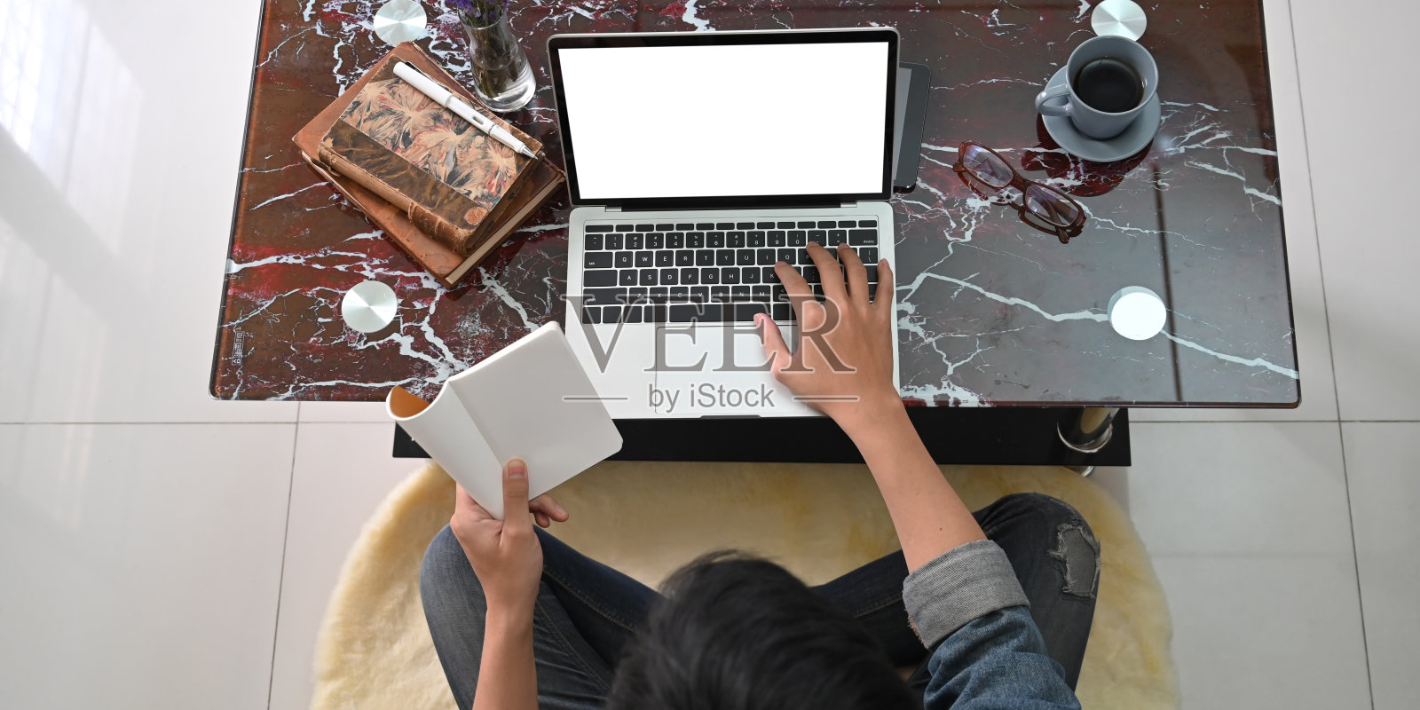 顶视图的形象，聪明的人工作，而坐在大理石纹理的桌子上，打字在他的原型电脑笔记本电脑在舒适的客厅。照片摄影图片