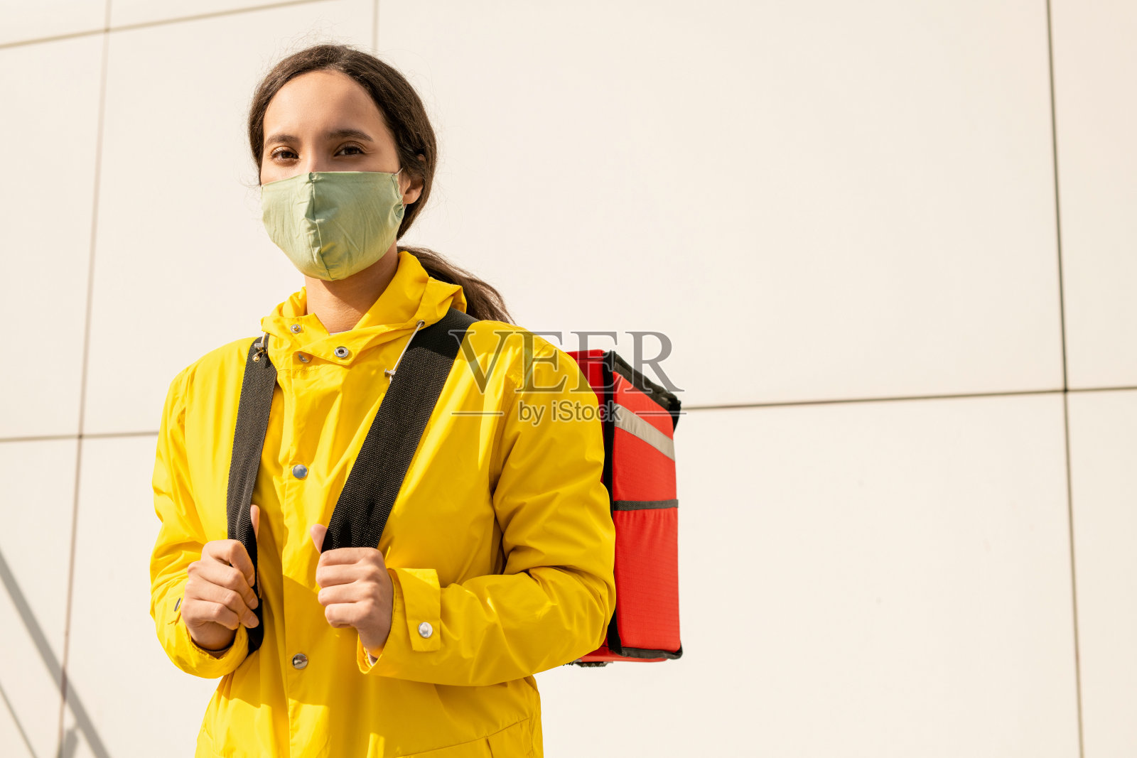 年轻的黑发快递在黄色夹克和保护面具拿着背包照片摄影图片