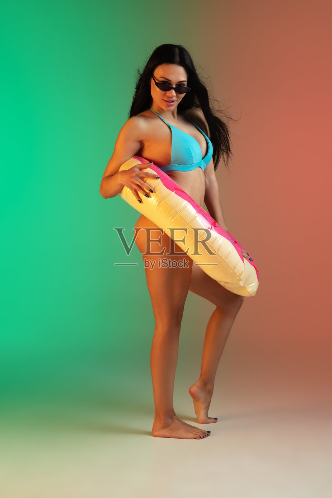 时尚肖像年轻的健康和运动的女人在蓝色奢侈泳衣与橡胶甜甜圈和时尚的太阳镜在梯度背景。完美的身材为夏天做好了准备。照片摄影图片