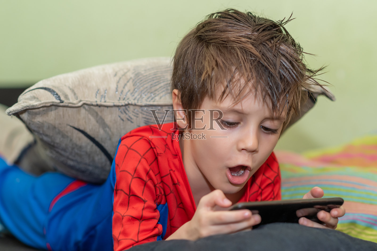 可爱的男孩拿着手机。在家里孤立无援感到无聊。照片摄影图片