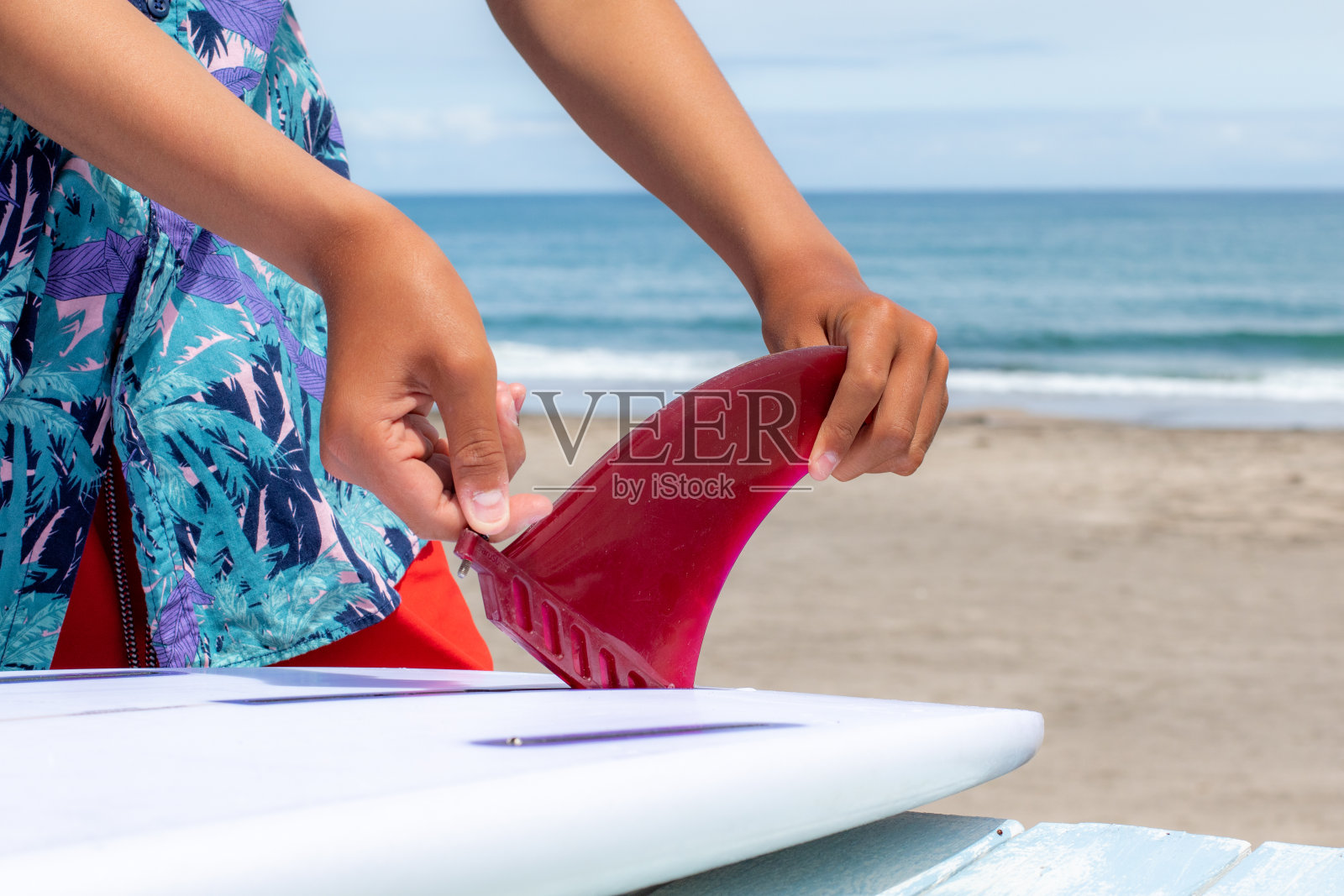 在日本，年轻的冲浪者把一个红色的冲浪板鳍放到一个白色的冲浪板上照片摄影图片