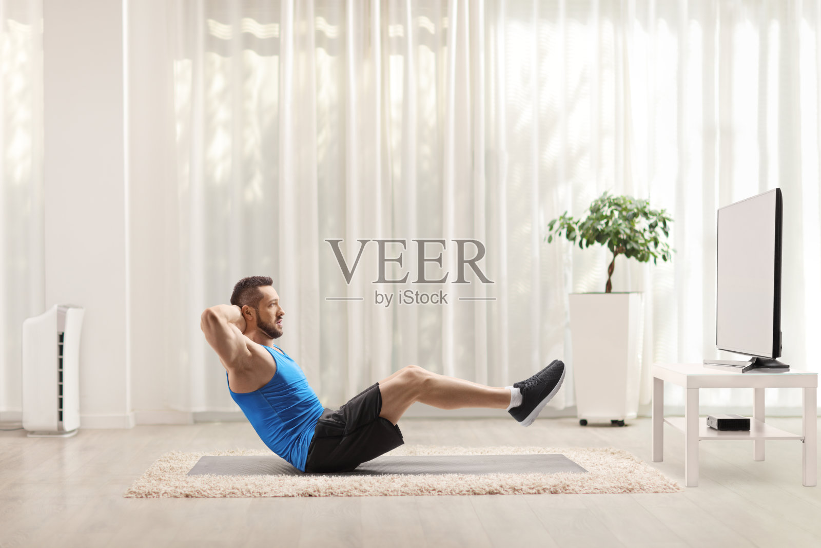 一个健康的年轻人在家看电视，在地板上锻炼腹肌照片摄影图片