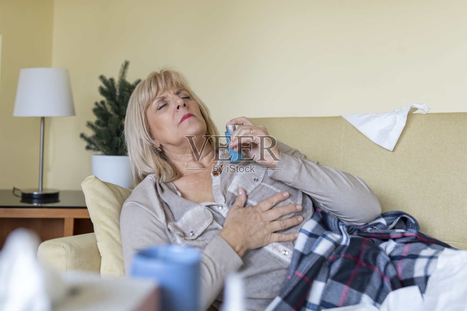 患有哮喘的老年妇女躺在床上使用吸入器。照片摄影图片