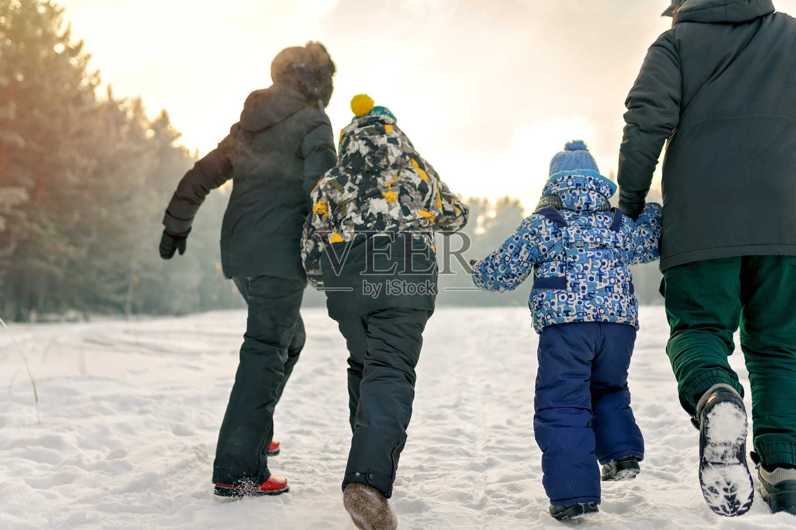 幸福的家庭:母亲，父亲和两个孩子在雪地上奔跑，在冬天的夕阳下照片摄影图片