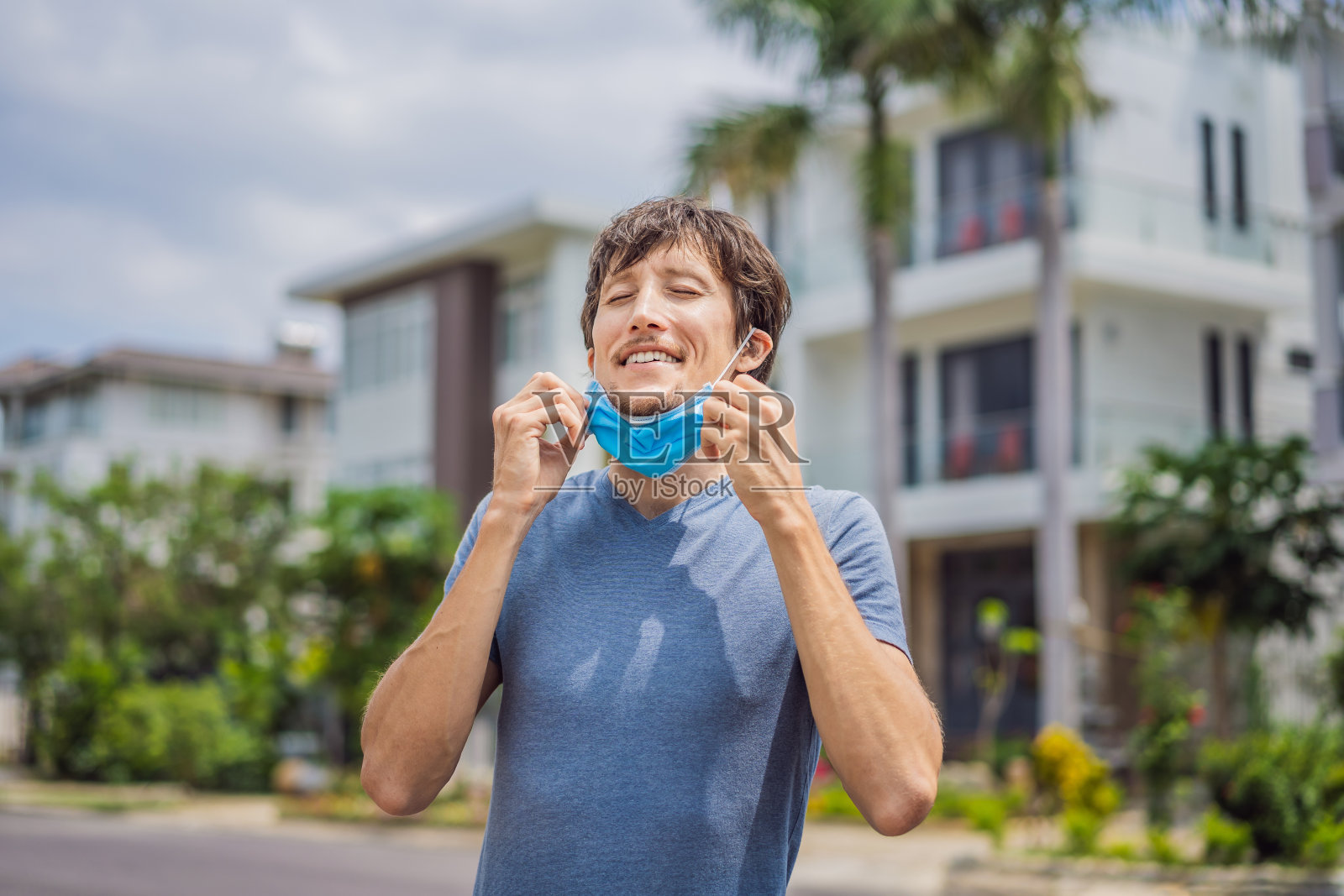 隔离已经过时了在小镇房屋的背景下，一名男子摘下面具。我们是安全的。冠状病毒结束。我们赢了。没有更多的隔离。呼吸深。摘下面具。冠状病毒已经结束照片摄影图片
