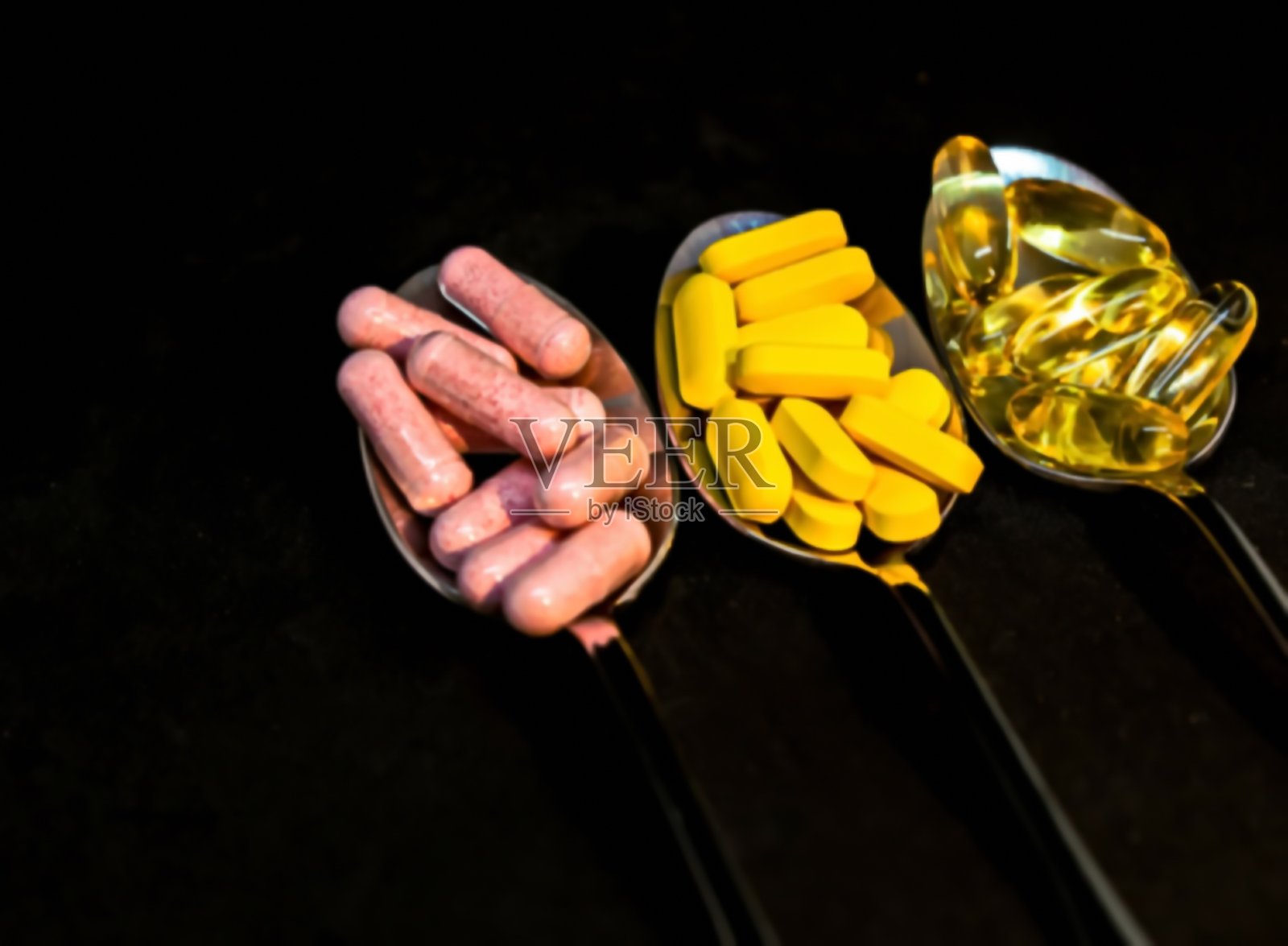 黑色背景上的三个勺子里的药丸 - 制药概念。模糊视图照片摄影图片