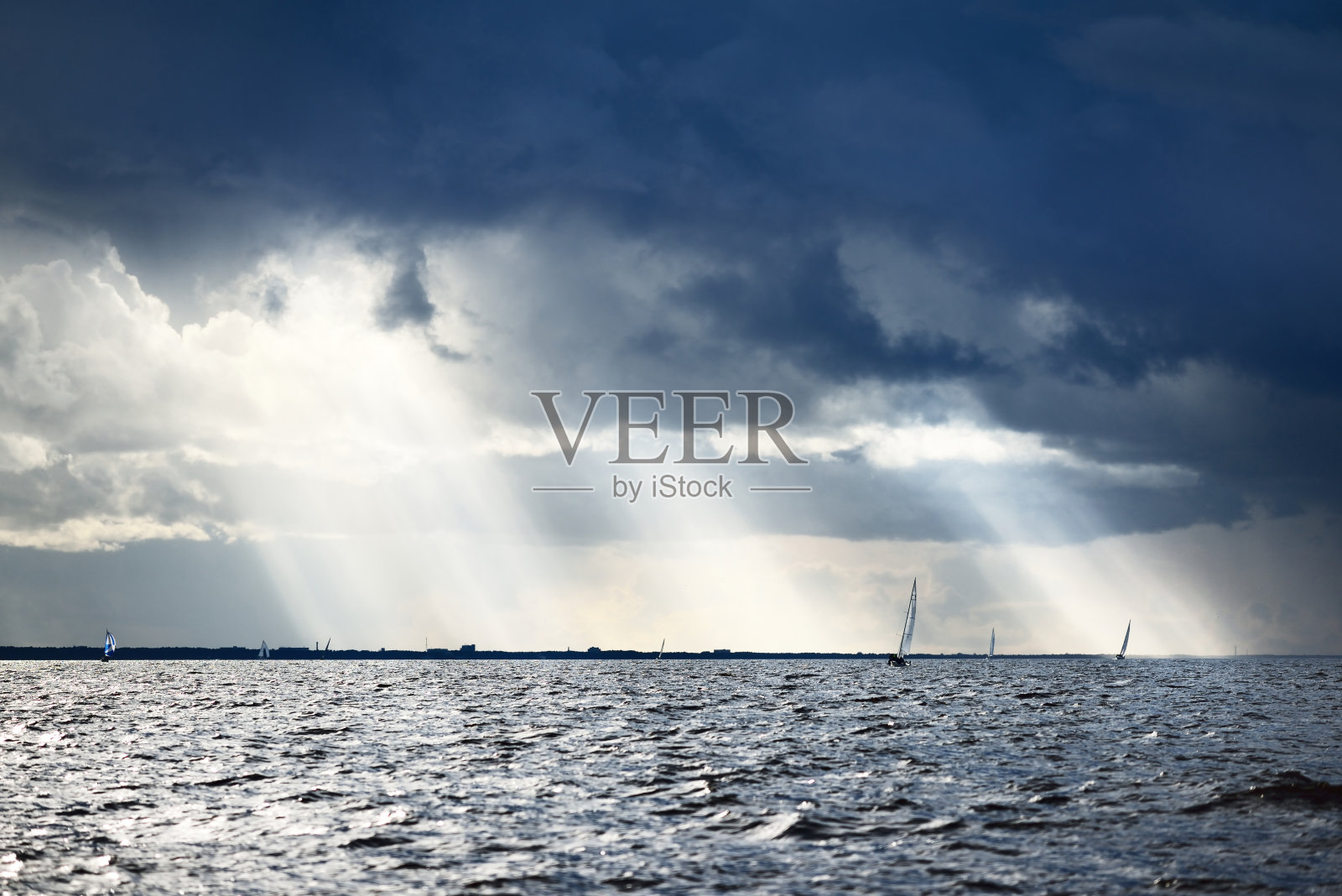 游艇赛舟会。在海浪中疾驰的现代帆船戏剧性的天空与流动的阳光在雷雨前。很棒的cloudscape。德国北部,基尔照片摄影图片