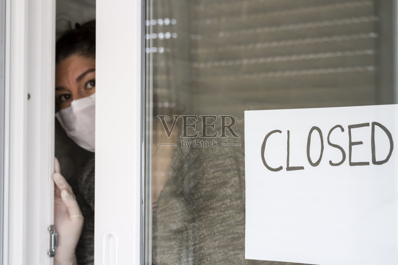 戴面具的员工在关门的商店里透过门看东西照片摄影图片