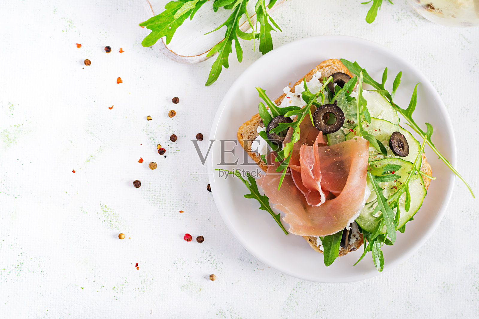 桌上有火腿、黄瓜、黑橄榄、芝麻菜和羊乳酪三明治。食品的趋势。俯视图，平放照片摄影图片