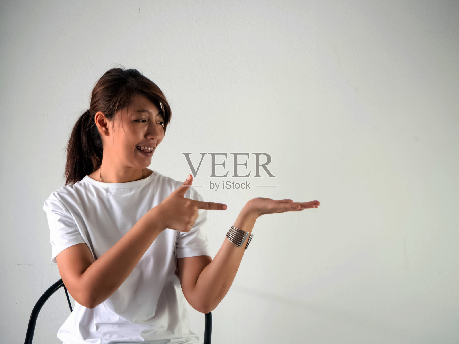 女人戴着背带，坐在椅子上，指着空空的手微笑。积极情绪照片摄影图片