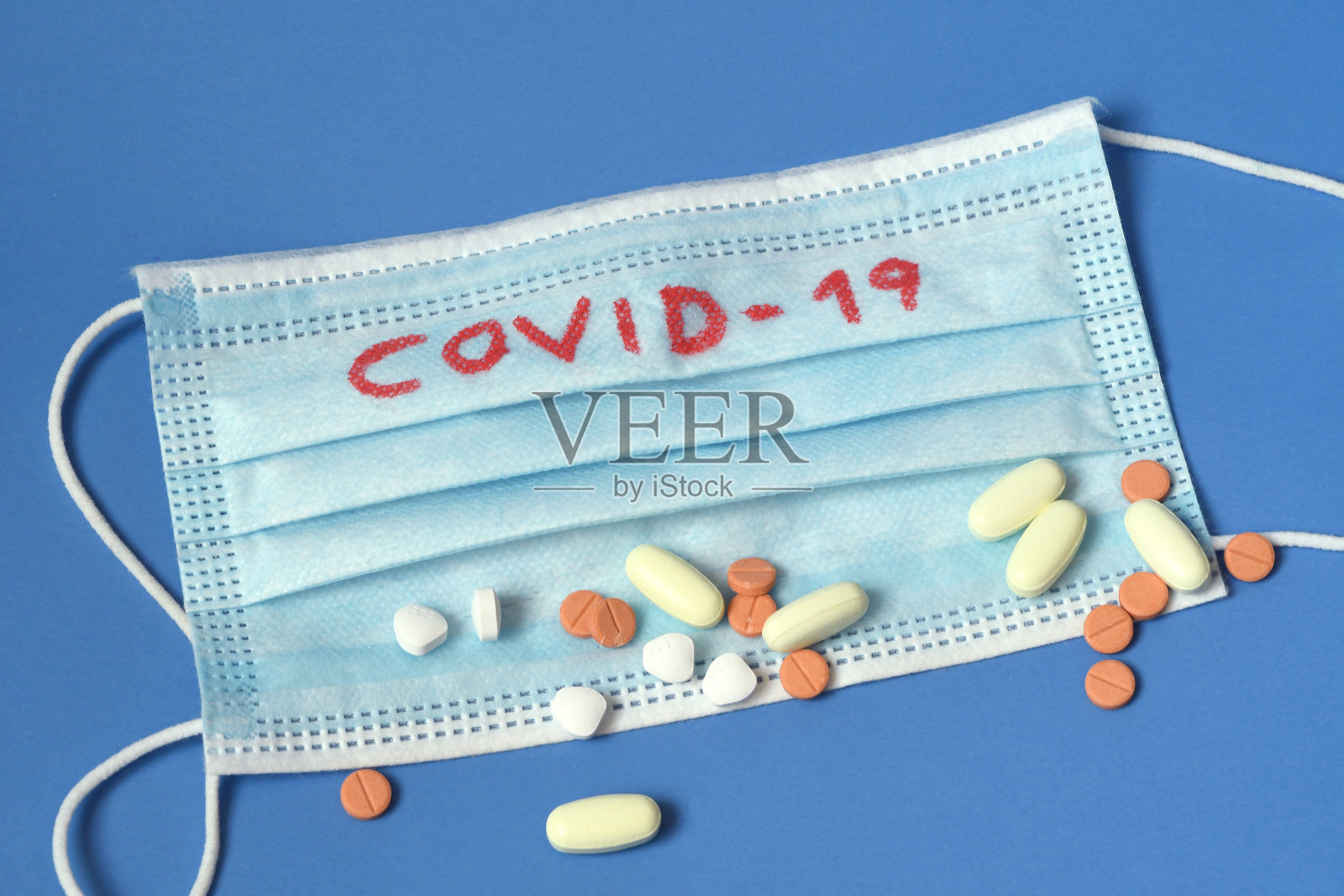 防毒外科口罩和蓝色背景的药品，上面有COVID-19字样。照片摄影图片