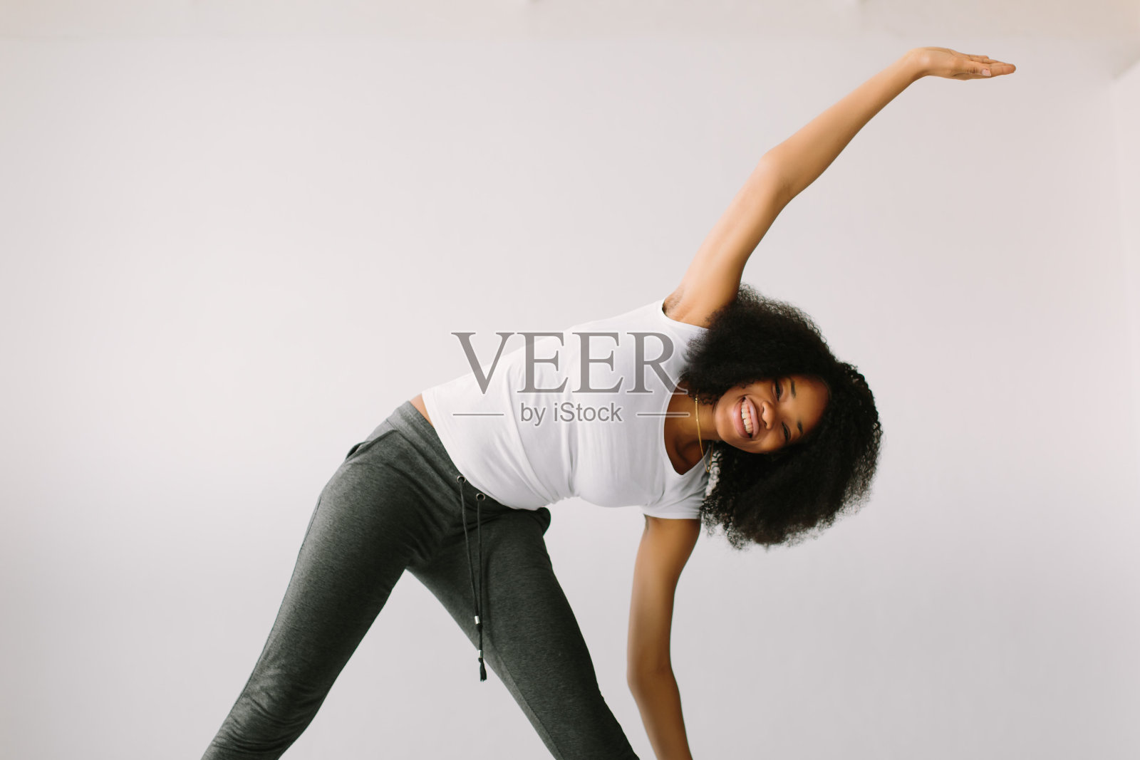 一位非裔美国年轻女子站在白色的床上做体育锻炼照片摄影图片