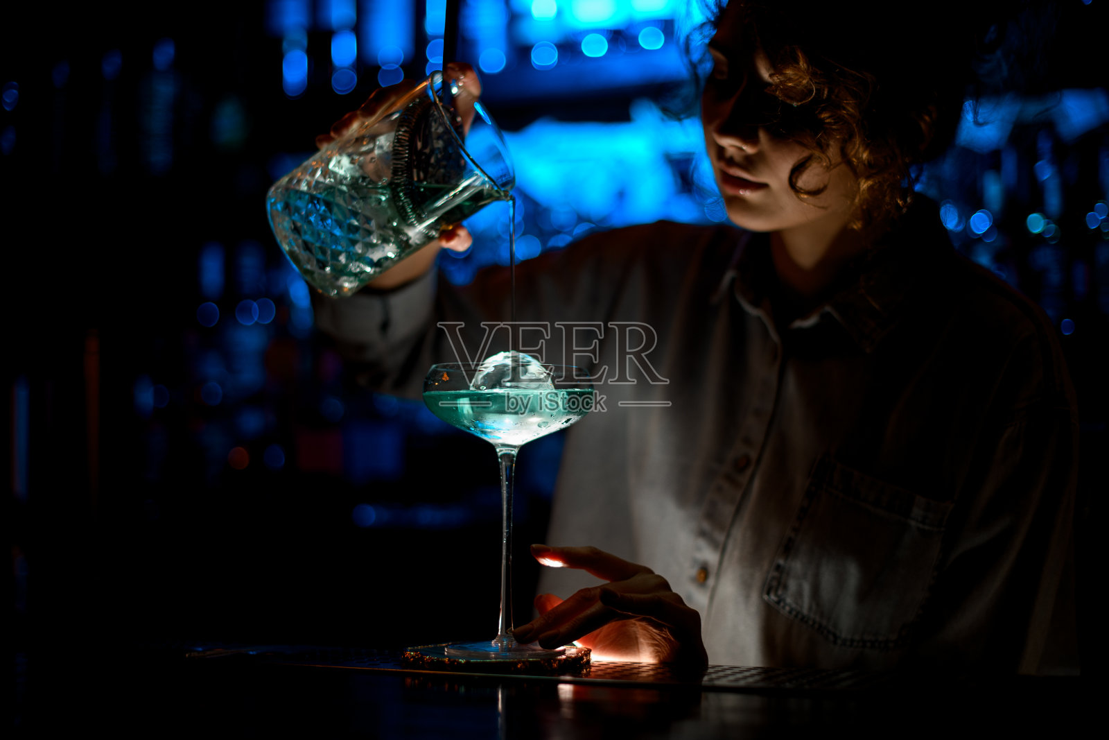 一个女人在酒吧里聚精会神地把鸡尾酒倒进玻璃杯里。照片摄影图片