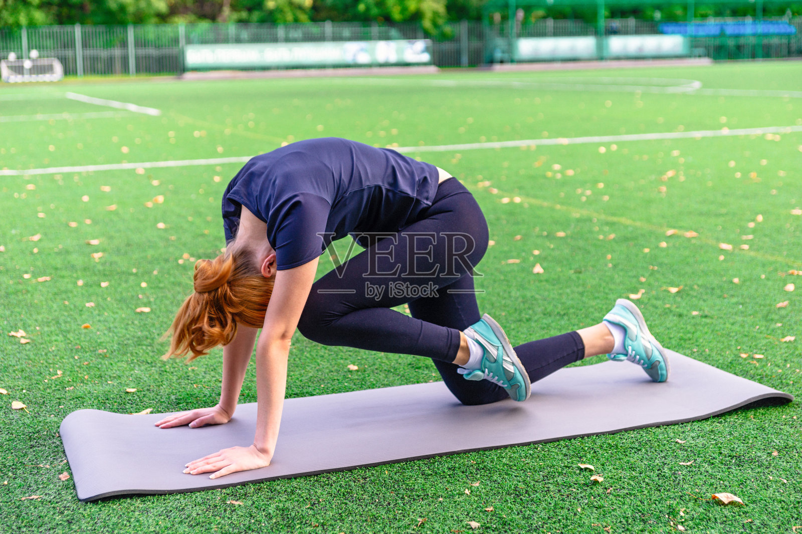 苗条美丽的女人在户外草地上的垫子上练习瑜伽。照片摄影图片