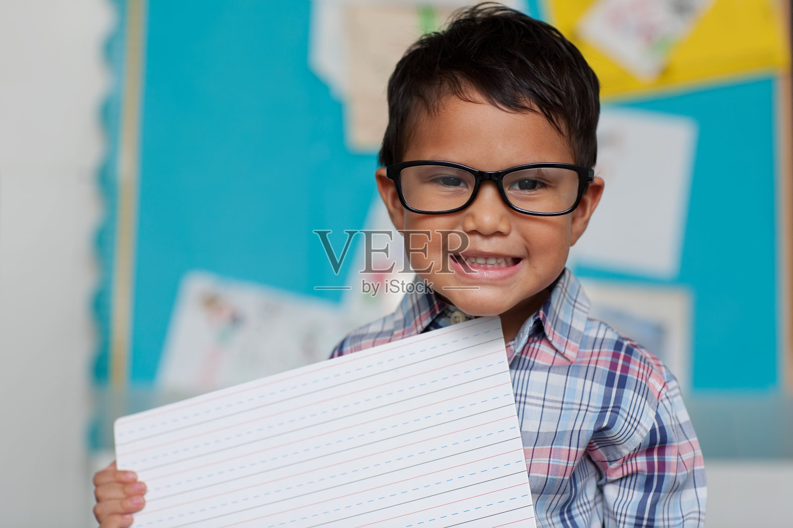 一个带着可爱微笑的小男孩，拿着一个书写指南板，戴着老花镜，穿着一件学院风的衬衫。照片摄影图片