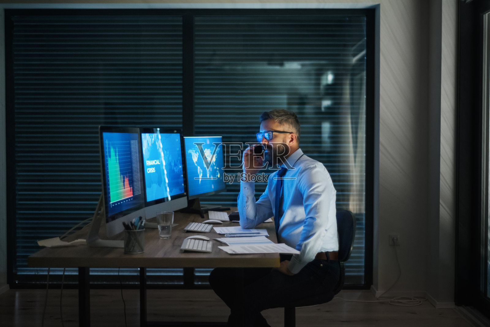 带着电脑坐在办公桌前工作到很晚。金融危机的概念。照片摄影图片