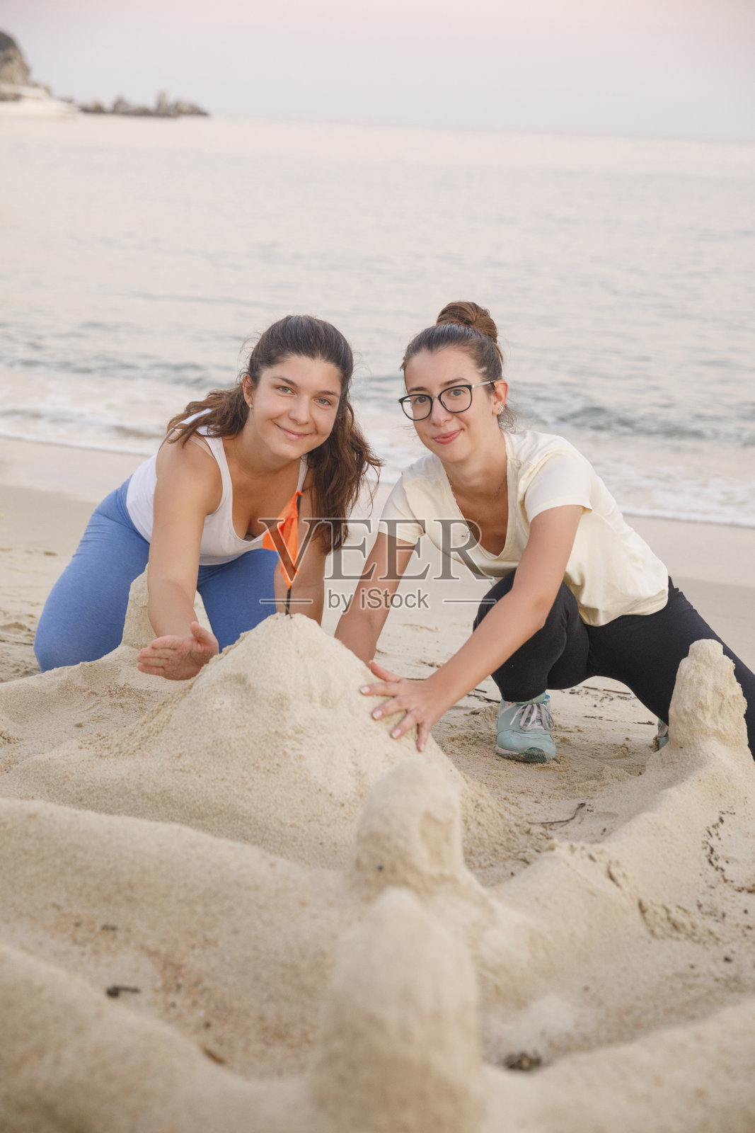 最好的朋友两个年轻的女人建造一座沙堡在海边的沙滩上放松。沙滩假日照片摄影图片
