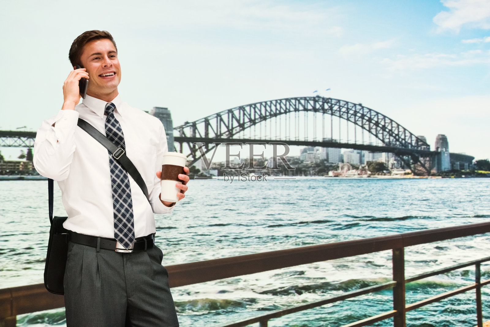 河边的年轻男性游客，穿着商务服装，手持咖啡杯，使用智能手机照片摄影图片