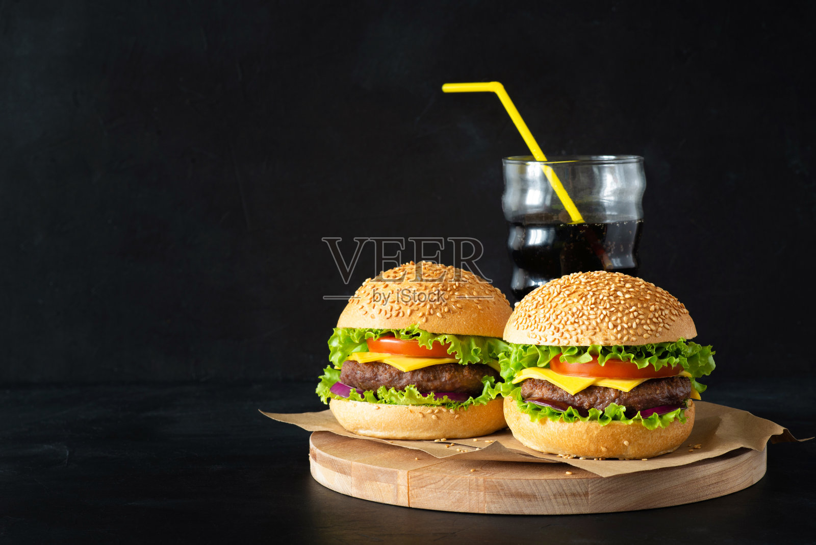 在黑色背景的小木板上，放上自制的汉堡、番茄酱和一杯可乐。照片摄影图片