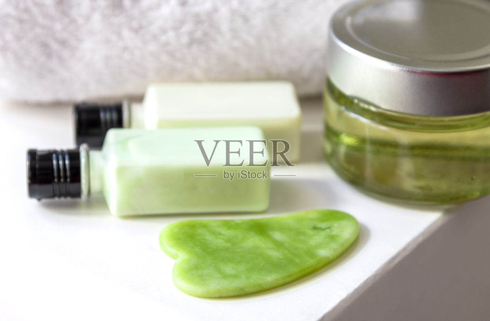 绿色刮痧工具，以化妆品为背景。有选择性的重点照片摄影图片