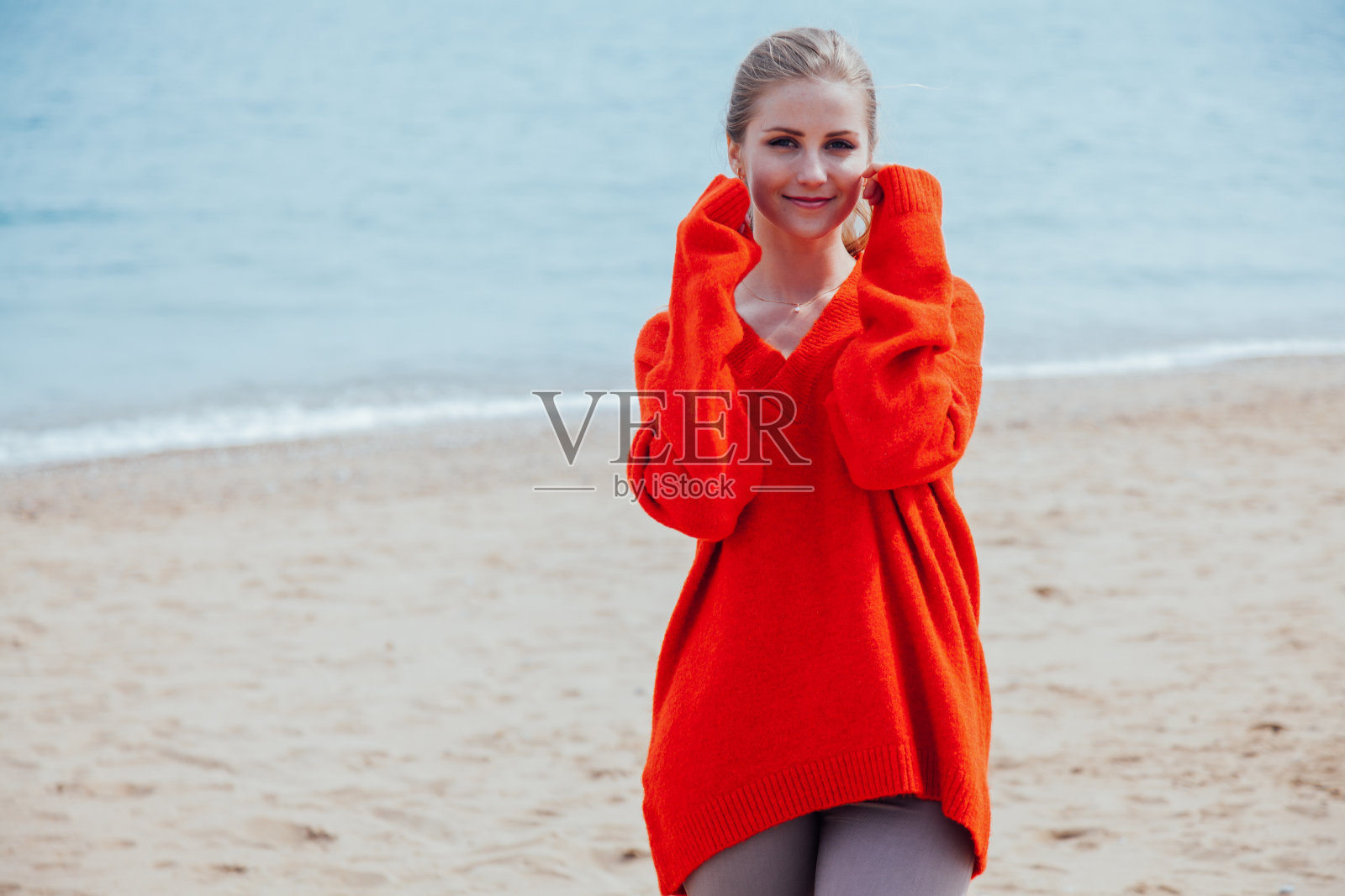 那个穿红衣服的金发女郎沿着海边的海滩散步照片摄影图片