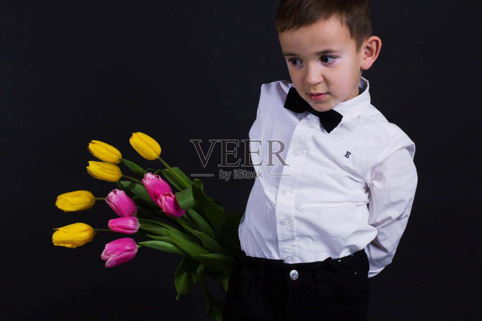 那个白癜风的男孩穿着白色衬衫，打着蝴蝶结，背景是黑色的Studio照片摄影图片