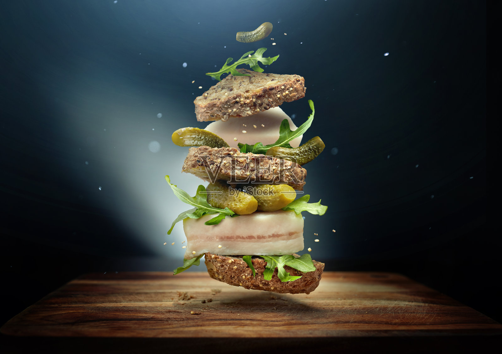 一种民间风格的三明治，在蓝色的背景上有一片培根，还有飞翔的配料泡菜和芝麻菜照片摄影图片