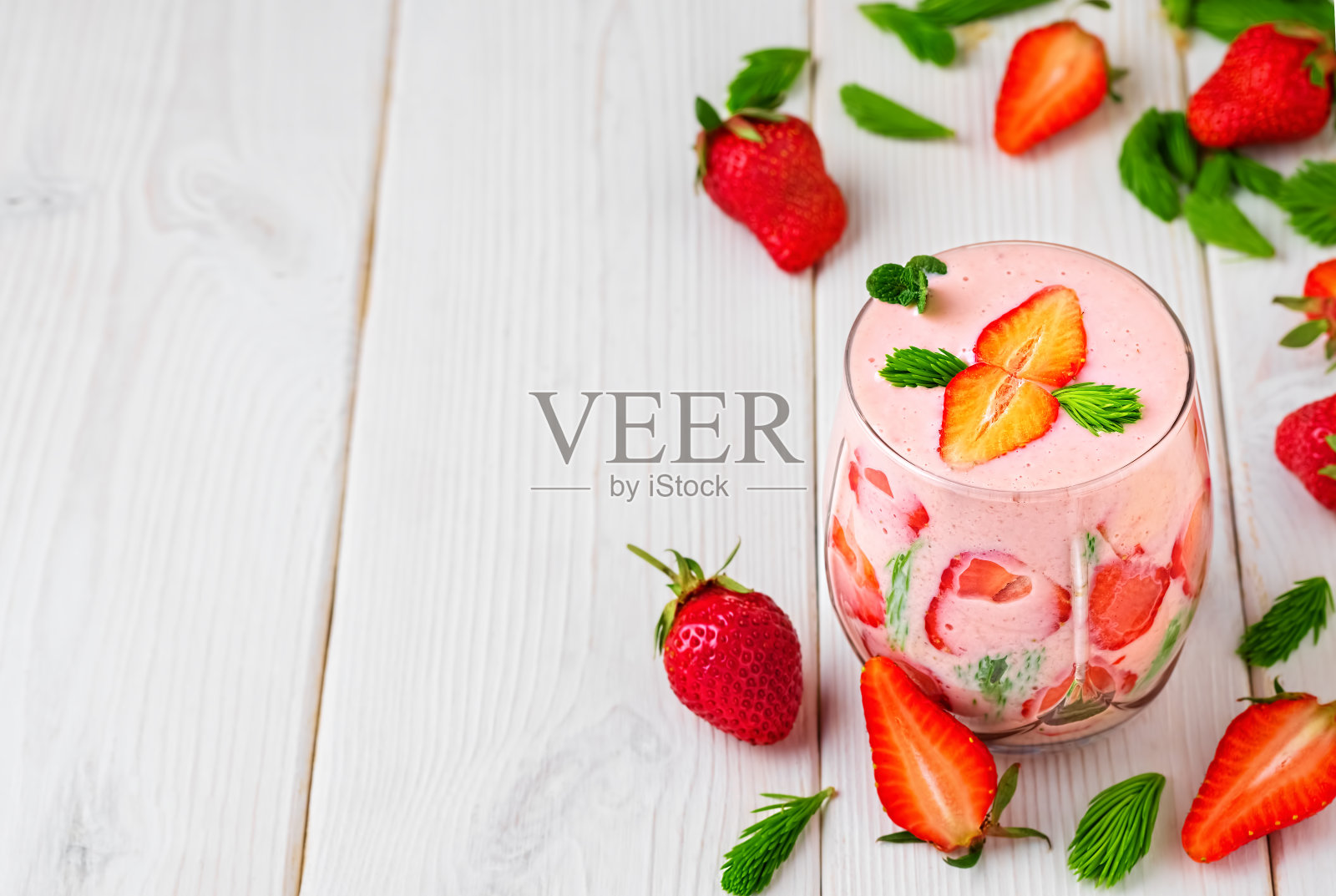 玻璃草莓鸡尾酒在白色的木制背景。桌上散落着草莓和云杉，是制作冰沙的原料。Smoothie顶视图与复制空间。照片摄影图片