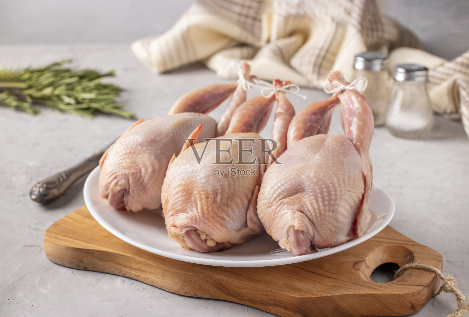 三只新鲜的鹌鹑放在木板上的白色盘子上，特写，灰色背景照片摄影图片