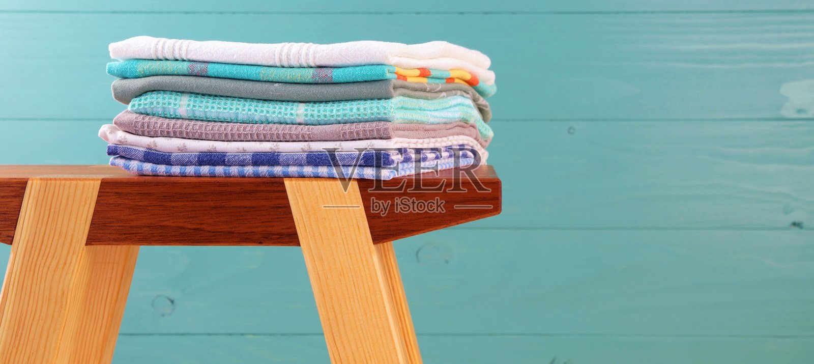 一堆亚麻厨房毛巾。彩色的洗碗毛巾堆叠在木制的工艺品凳子上，在木制的背景下。空白的文本复制空间。照片摄影图片