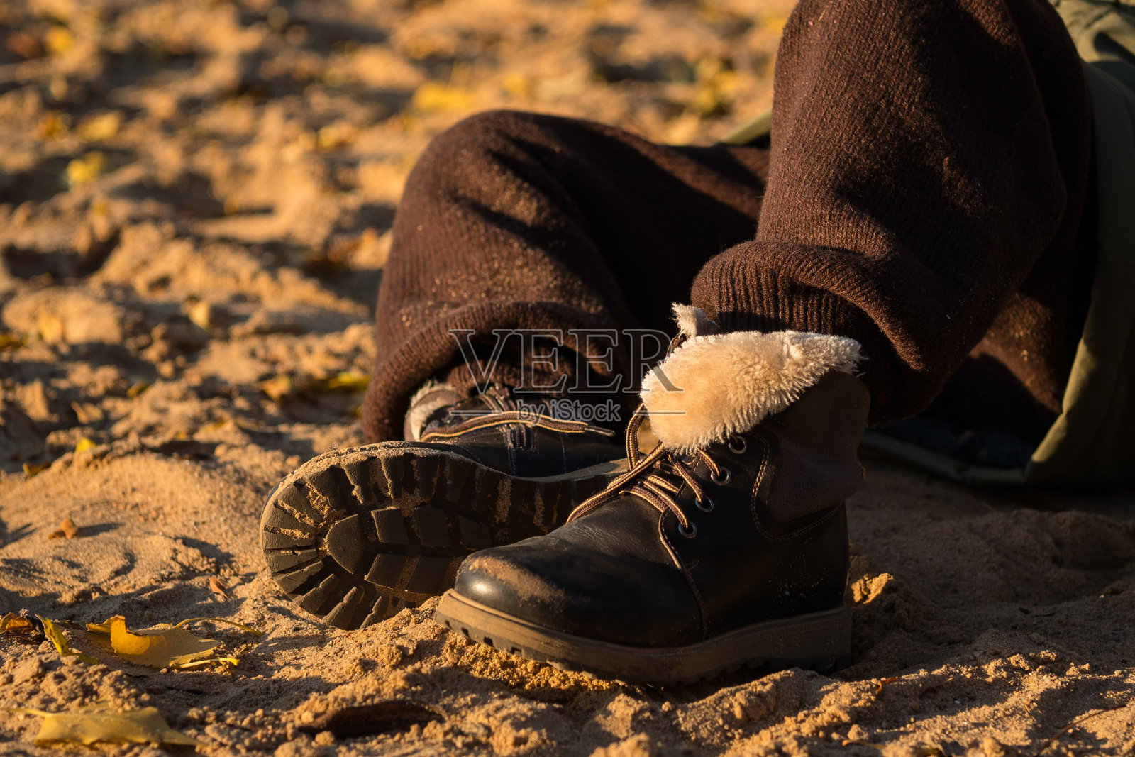 一个男孩的脚特写，他穿着棕色的裤子和皮靴，金色的沙子和夕阳的光线，衣服上的沙子，照片摄影图片