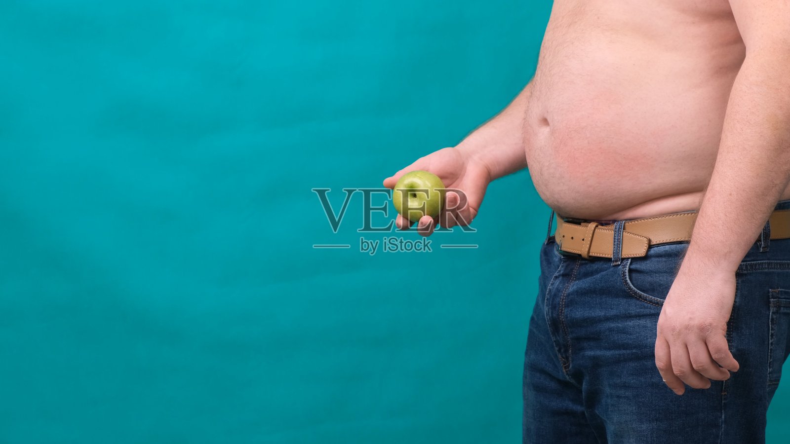 一个大肚子的胖子手里拿着一个青苹果。健康饮食与减肥的概念，饮食照片摄影图片