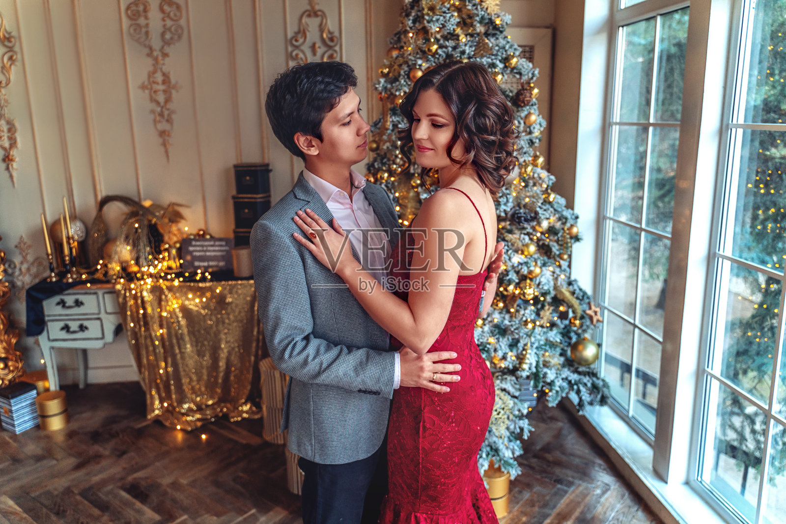 在圣诞树的背景下，情侣们穿着优雅的衣服一起迎接新年或圣诞节照片摄影图片