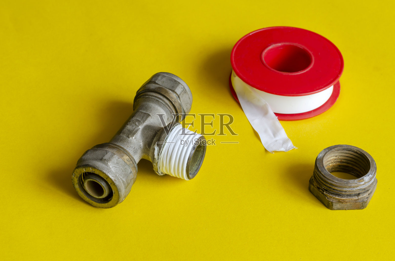 水三通分配器，螺母和密封胶带在黄色背景。照片摄影图片