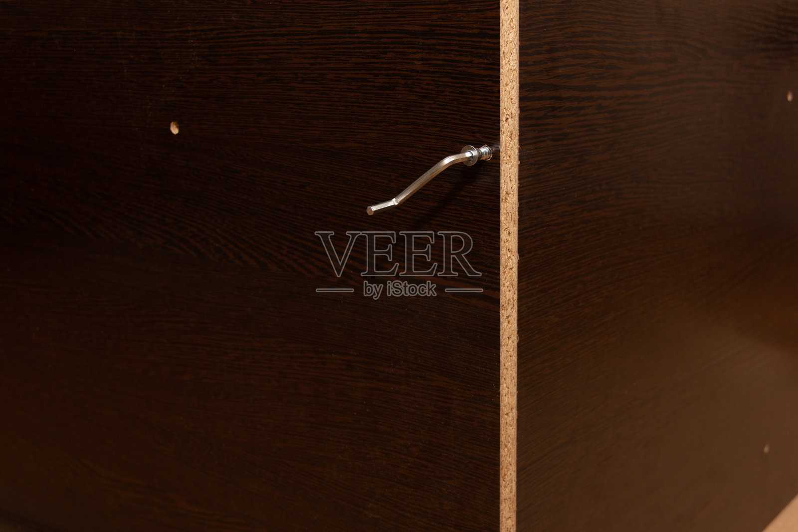 家具内六角键上有一颗螺钉，背景为深棕色的新拼装家具，由层压刨花板制成照片摄影图片