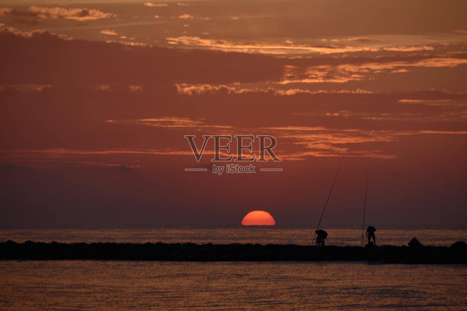 太阳出现在防波堤上的渔民中间照片摄影图片