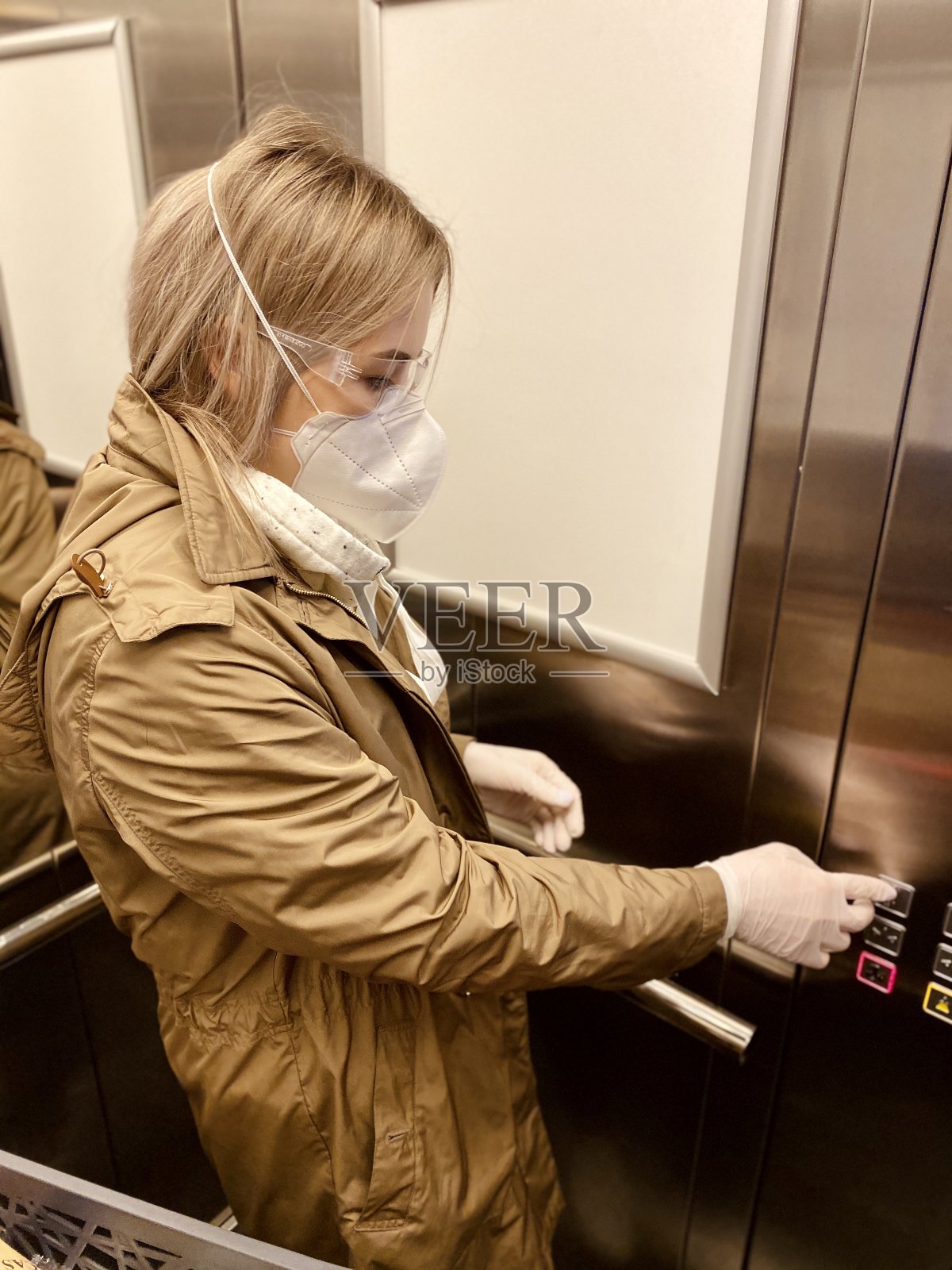 年轻女子戴上防护流感口罩、护目镜和手套，按下电梯按钮。购物在冠状病毒。照片摄影图片